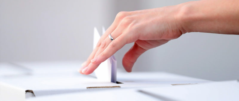 a person putting a ballot into a ballot box